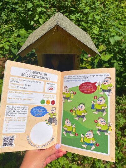 Ein Wanderpass für den Barfußpfad im Bolsdorfer Tälchen wird in der Hand gehalten, mit Illustrationen und Informationen zur Wanderung.