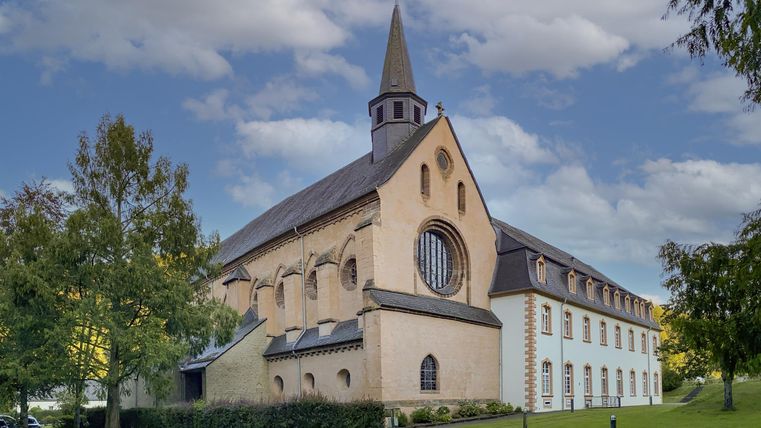 Une église impressionnante avec un clocher pointu et de grandes fenêtres. Entourée d'espaces verts et d'un ciel clair.