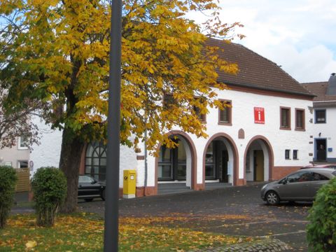 Ein historisches Gebäude mit weißen Wänden und Bögen. Im Vordergrund steht ein Baum mit herbstlichen Blättern.