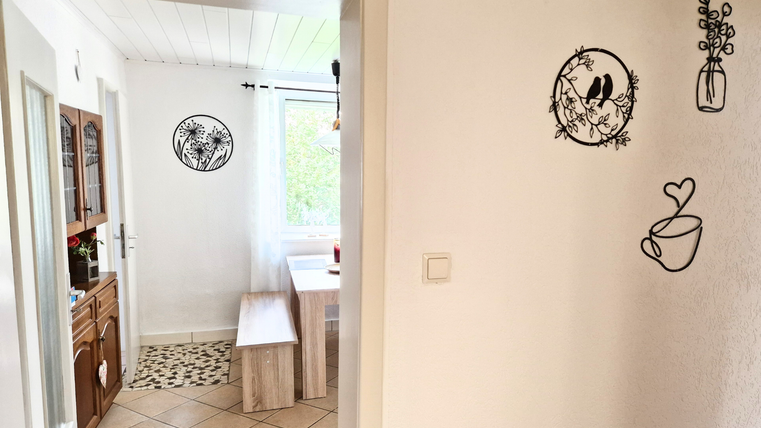 Un couloir lumineux avec une décoration murale et une vue sur un coin repas confortable. Sur le côté gauche, on peut voir un coin cuisine.