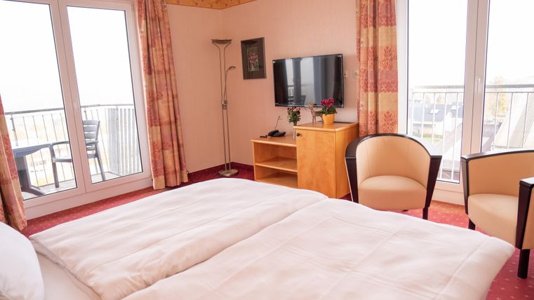 A cozy hotel room with a double bed and a television. Large windows provide plenty of daylight and a view outside.