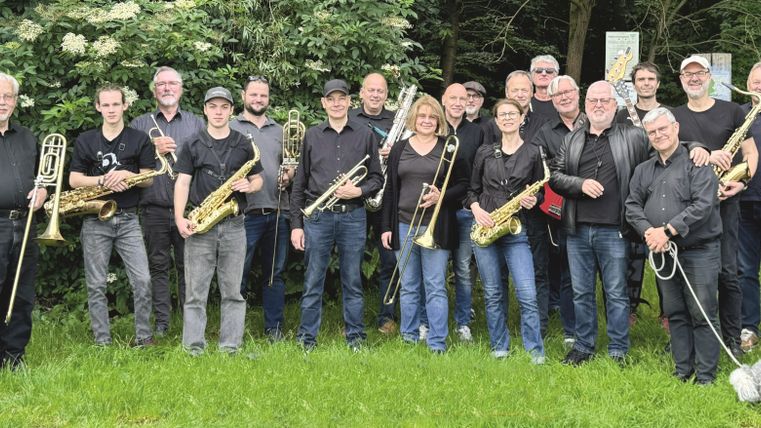 <p>Gruppenfoto der Band. Alle Mitglieder stehen nebeneinander und halten stolz ihre Instrumente in der Hand</p>