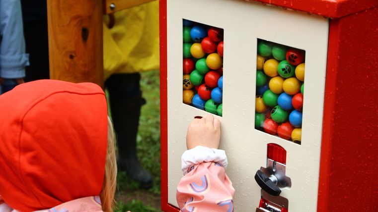 Ein Kind steht vor einem Kugelautomaten und zieht sich eine Kugel daraus.