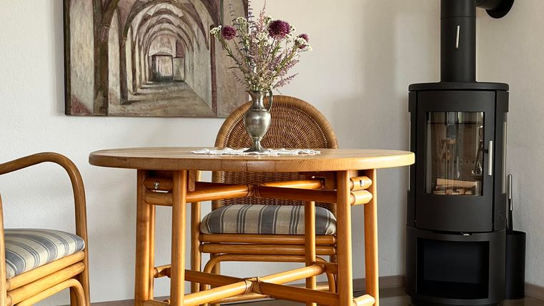 Une pièce confortable avec une table ronde et deux chaises. Au mur, il y a une image et un poêle moderne est placé dans le coin.
