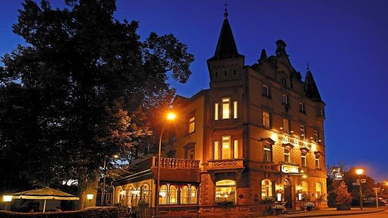 Un bâtiment historique magnifiquement éclairé la nuit. Des arbres et des lampadaires entourent la façade.