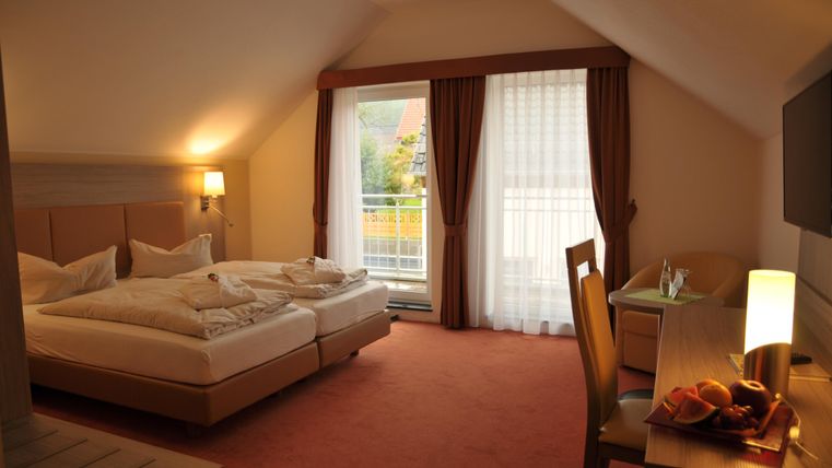 Une chambre d'hôtel confortable avec deux lits et un bureau. De grandes fenêtres laissent entrer beaucoup de lumière naturelle et offrent une vue sur l'extérieur.