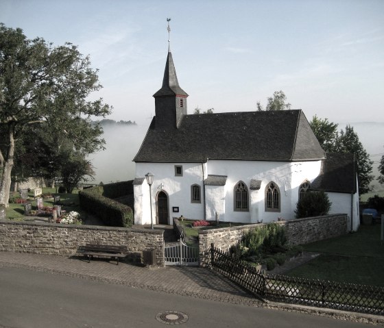Wei&szlig;e Kapelle in Kerschenbach, umgeben von einem Friedhof und B&auml;umen. Nebel liegt im Hintergrund, was eine ruhige Atmosph&auml;re schafft., &copy; OG Kerschenbach