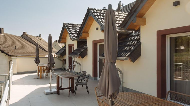 Eine moderne Terrasse mit Tischen und Stühlen. Die Sonnenschirmen bieten Schatten an einem klaren Tag.