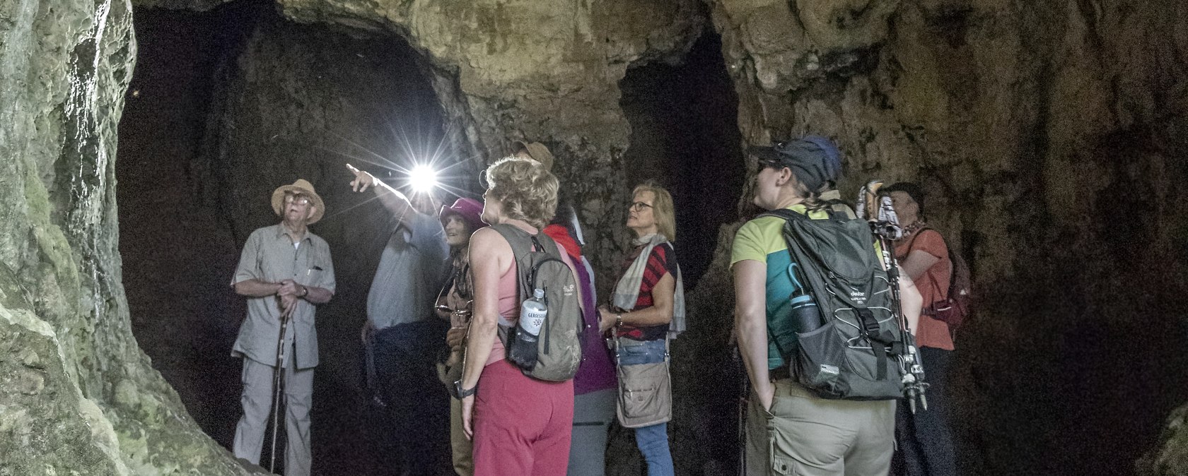 Eine Wandergruppe von etwa 10 Personen steht im Innenraum einer großen Höhle. Die Personen bestaunen die massiven Steinwände um sie herum.