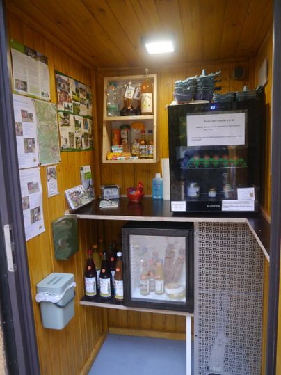 Kleiner Verkaufsraum mit Holzverkleidung, Regalen mit Getränken, Eiern und anderen Produkten. An der Wand hängen Informationsblätter.