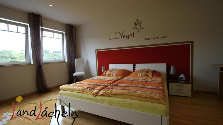 Ein modernes Schlafzimmer mit einem Doppelbett und bunten Bettdecken. Große Fenster lassen viel Licht herein und sorgen für eine einladende Atmosphäre.