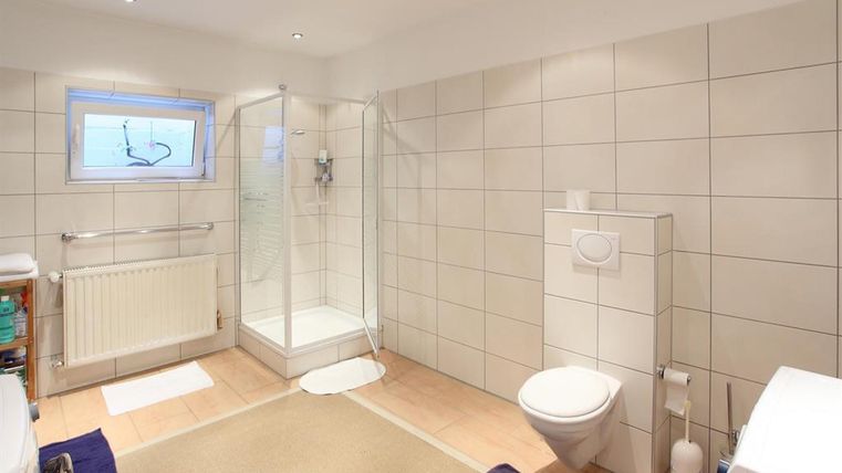 Ein modernes Badezimmer mit einer Dusche, einem WC und hellen Fliesen. Das Licht fällt durch ein Fenster und der Raum wirkt sauber und einladend.