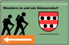Sign with two hikers, a coat of arms and an arrow pointing left. Text: "Hiking in and around Gönnersdorf" and website link., © Touristik GmbH Gerolsteiner Land