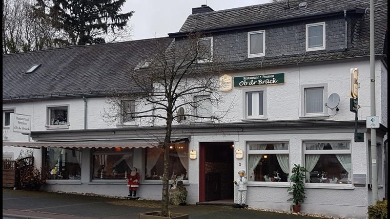 Das Restaurant mit dem Namen 'Ob dr Brück', dekoriert mit Weihnachtsfiguren, in einem grauen Gebäude mit Schieferdach.