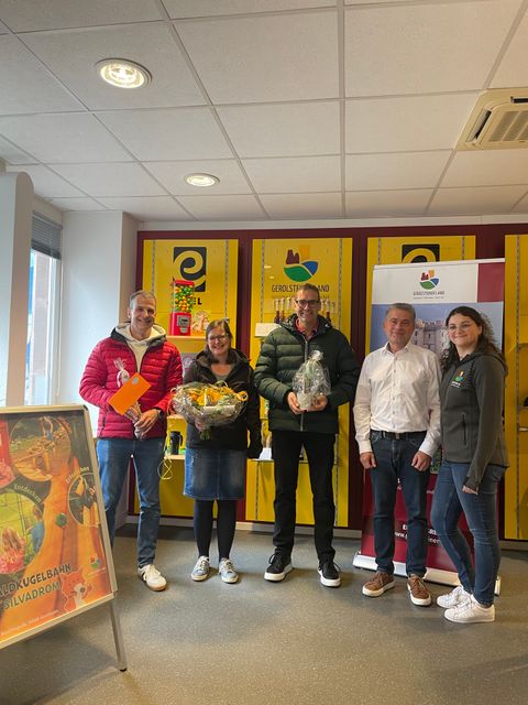 5 Personen stehen nebeneinander vor einem Souvenierregal in der Tourist-Information Gerolstein und lachen in die Kamera. 3 der Personen halten stolz Preise in den Händen.