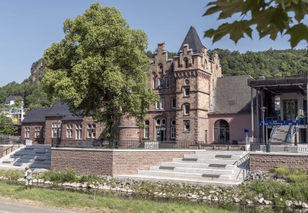 Exterior fa&ccedil;ade of Gerolstein railway station with stairs and lift providing access to the platforms behind a densely overgrown tree and next to the River Kyll.