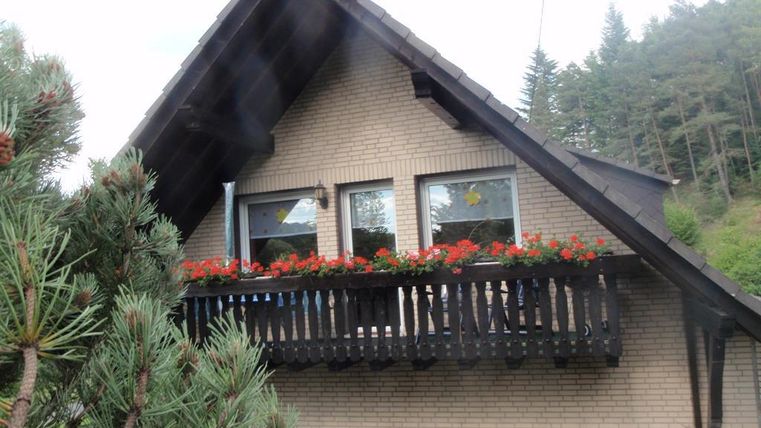 Ein gemütliches Haus mit einem Balkon, der mit roten Blumen geschmückt ist. Im Hintergrund sind Bäume zu sehen.