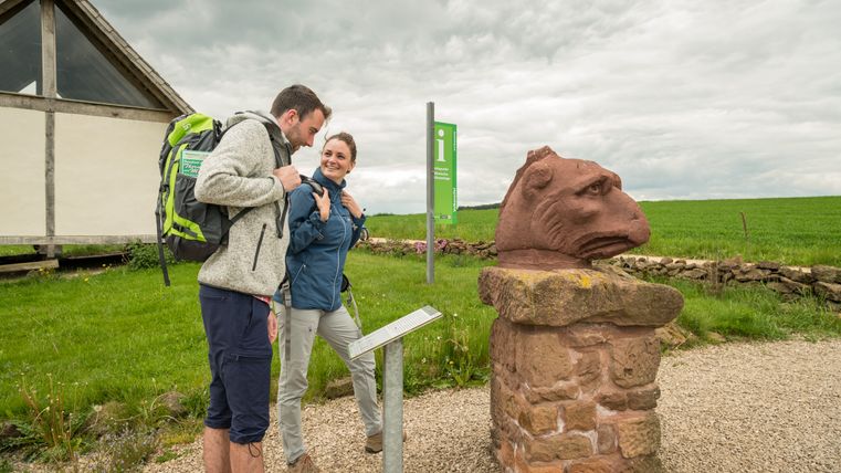 Twee wandelaars bekijken een stenen sculptuur op een wandelpad in de Eifel.