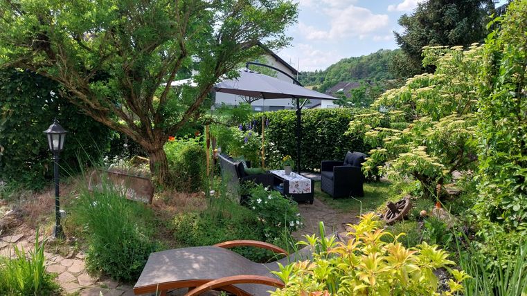 Een uitnodigende tuin met veel groen en gezellige zitjes. Ligbedden en een schaduwrijke prieel zorgen voor een ontspannen sfeer.