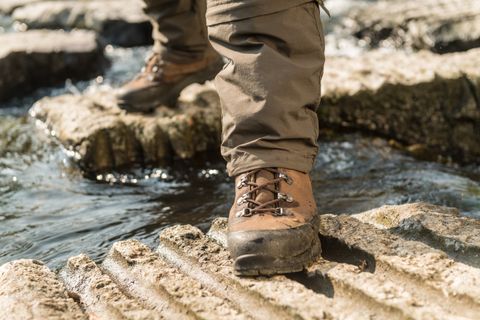 Close-up of a hiking boot on a rock above a flowing stream.