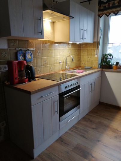 Een moderne keuken met houten kasten en een fornuis. Op de achtergrond zijn decoratieve tegels en een vensterbank met planten te zien.