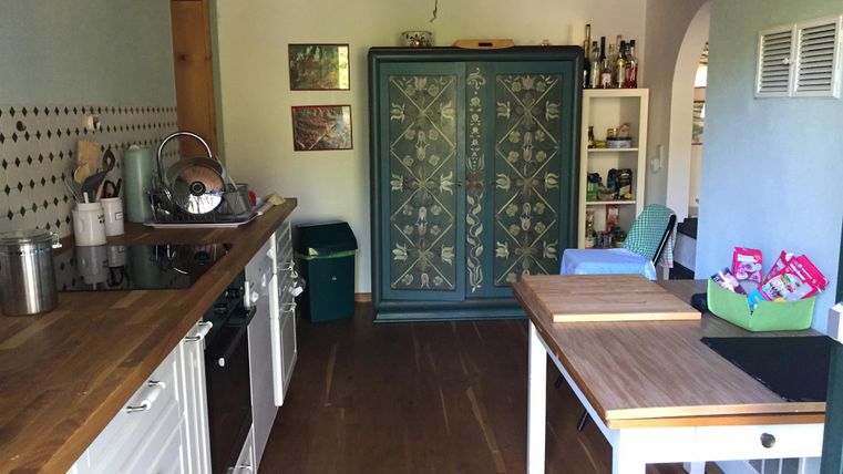 Een gezellige keuken met houten planken en een grote, decoratieve kast. Op het aanrecht zijn keukengerei en voedsel zichtbaar.