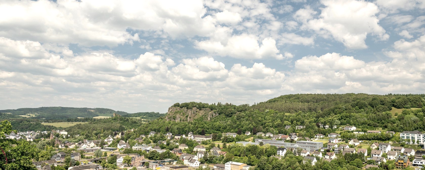 Panoramic view of Gerolstein with green hills, houses and a cloudy sky. The landscape is surrounded by lush vegetation., &copy; Eifel Tourismus GmbH, Dominik Ketz