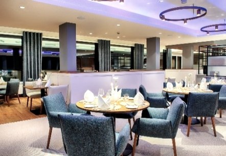Modern restaurant with blue sofa chairs at round tables, stylishly laid.