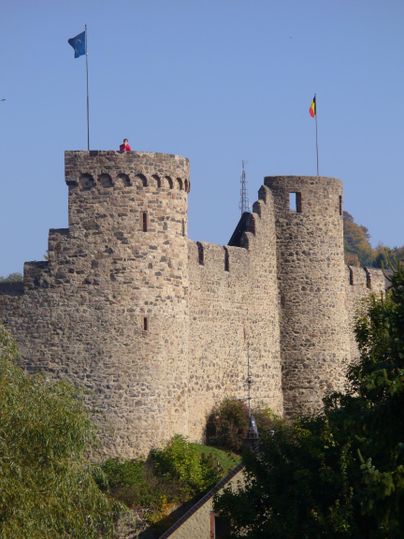 Die Stadtmauer von Hillesheim mit zwei runden Türmen, auf denen Flaggen wehen. Ein klarer blauer Himmel im Hintergrund.