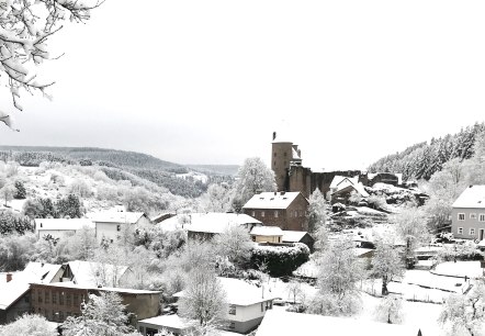 Blick auf eine verschneites Dorf. Eine große Burg ragt zwischen den mit Schnee bedeckten Häusern hervor.