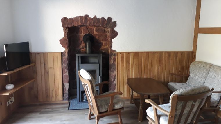 Ein gemütlicher Wohnraum mit Holzbalken und einer modernen Heizung. Die Einrichtung besteht aus einem Fernseher, einem Tisch und bequemen Sesseln.