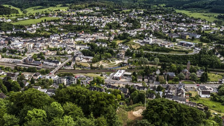 Eine malerische Stadtlandschaft mit grünen Hügeln im Hintergrund. Die Straßen und Gebäude sind gut sichtbar und verleihen der Szene eine ruhige Atmosphäre.
