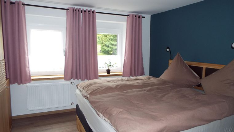 Ein gemütliches Schlafzimmer mit einem großen Bett und rosa Vorhängen. Der Raum hat eine blaue Wand und ein Fenster mit Blick ins Freie.