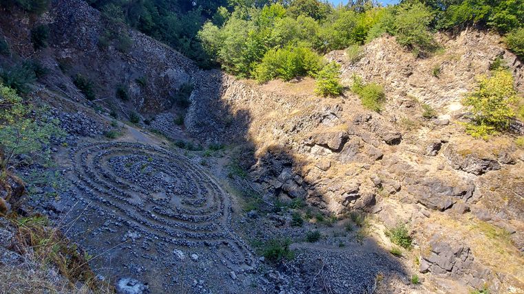 Steinlabyrinth in der felsigen Grube des Arensberg Vulkans mit Bäumen im Hintergrund.