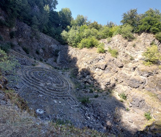 Stone labyrinth in the rocky pit of the Arensberg volcano, surrounded by trees and blue sky., © Touristik GmbH Gerolsteiner Land