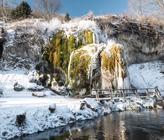Verschneiter Wasserfall Dreimühlen mit Moos und Eis, umgeben von kahlen Bäumen und blauem Himmel., © Rheinland-Pfalz Tourismus GmbH, Dominik Ketz