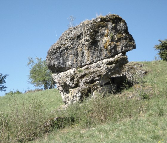 A large, moss-covered rock stands on a green meadow under a clear blue sky., © Touristik GmbH Gerolsteiner Land