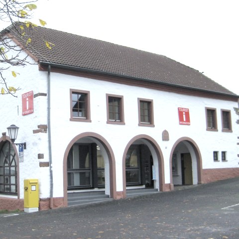 Exterior fa&ccedil;ade of the Stadtkyll Tourist Information Centre in the historic market barn with street and car park in front.