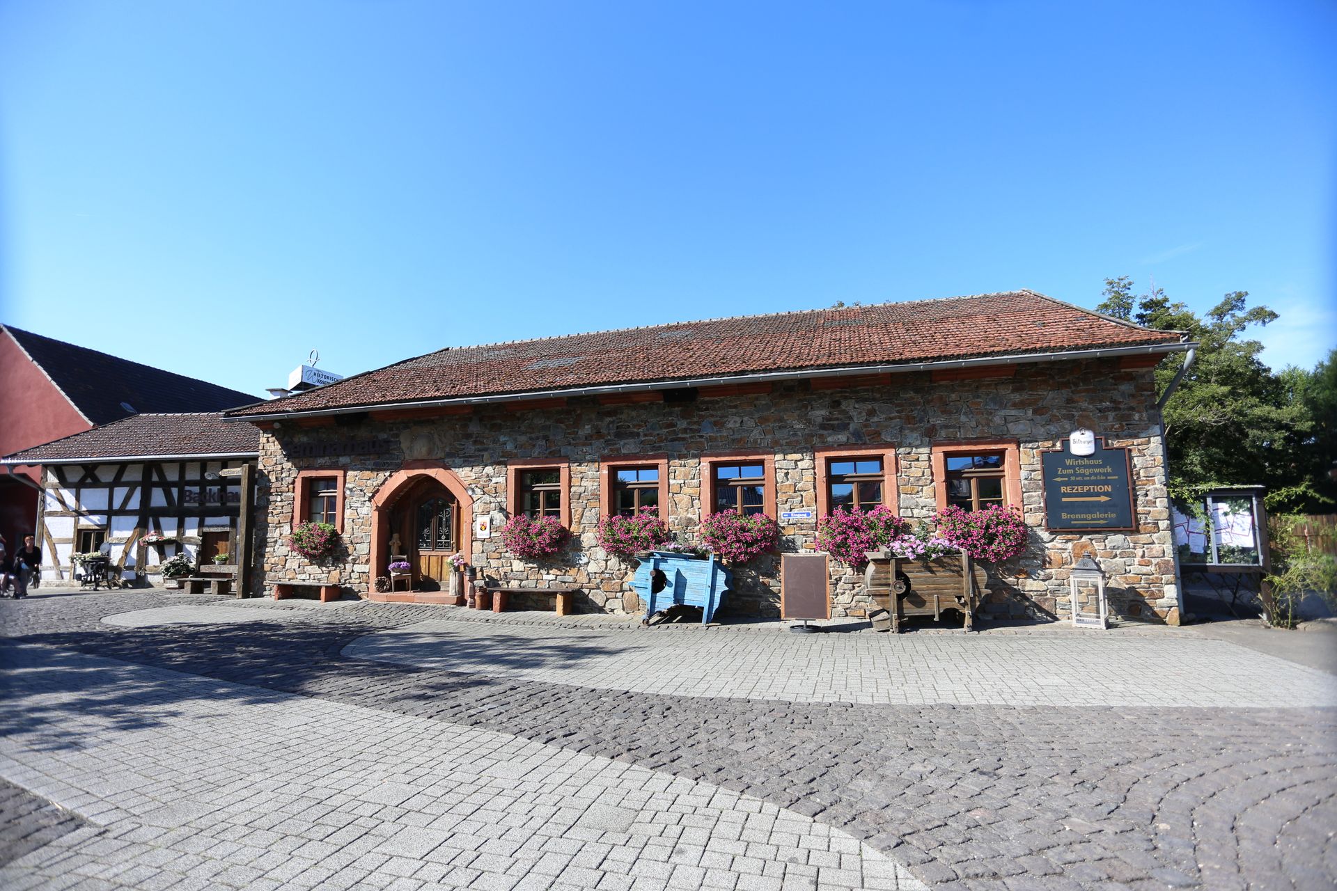 Eine historische Wassermühle aus Backstein mit mehreren Fenstern und einem gepflasterten Vorplatz.