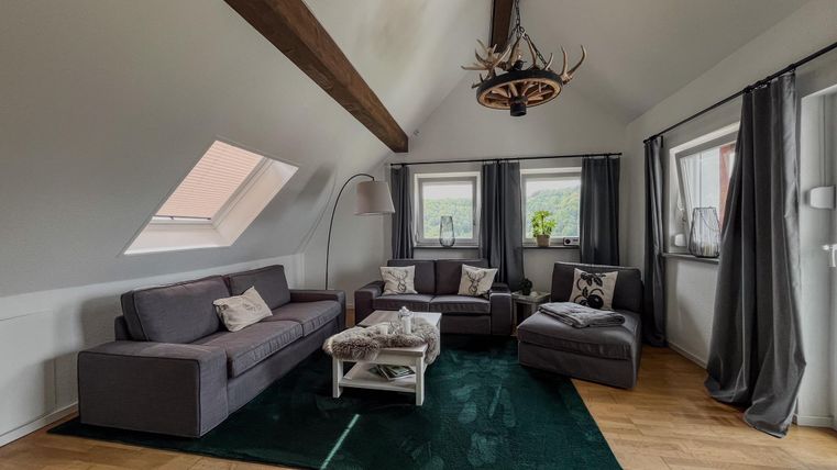 Ein modernes Wohnzimmer mit grauen Sofas und einem eleganten Couchtisch. Große Fenster sorgen für viel Tageslicht und eine gemütliche Atmosphäre.