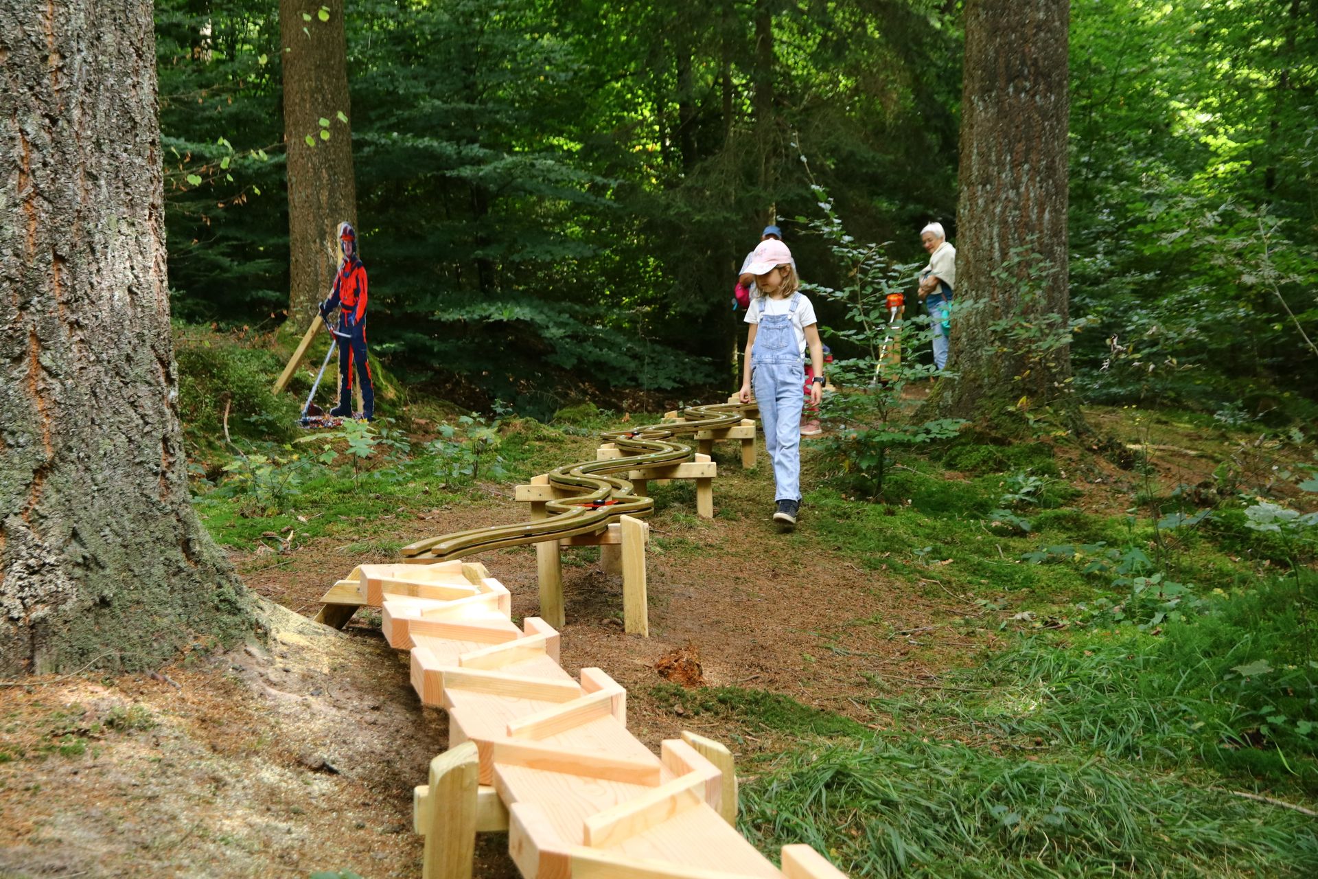 Kinder spielen an einer hölzernen Kugelbahn im Wald.