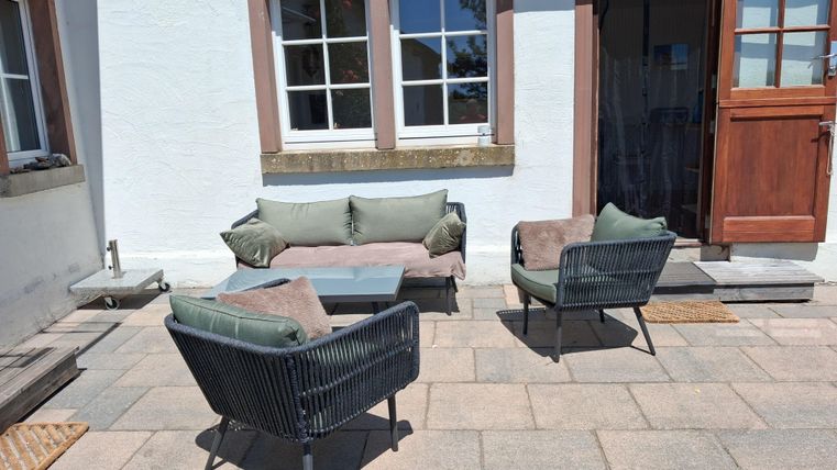Eine gemütliche Terrasse mit modernen Sitzmöbeln. Die Sonnenstrahlen scheinen durch die Fenster und schaffen eine einladende Atmosphäre.