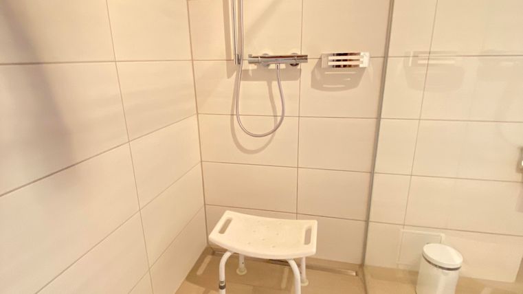 Eine moderne Dusche mit weißen Fliesen und einem Duschstuhl. Der Raum wirkt sauber und hell.