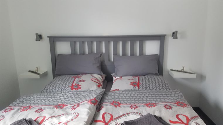 Ein gemütliches Schlafzimmer mit einem grauen Doppelbett und frischen Bettwäsche. An den Wänden befinden sich kleine Regale mit sanften Lichtquellen.