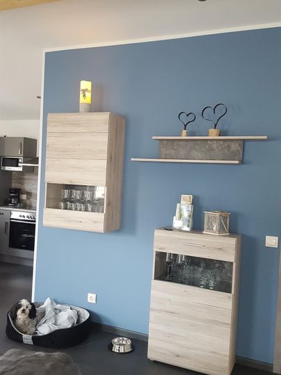 Ein modernes Wohnzimmer mit blauen Wänden und Holzdetails. Es gibt einen Hundekorb und stilvolle Möbelstücke.