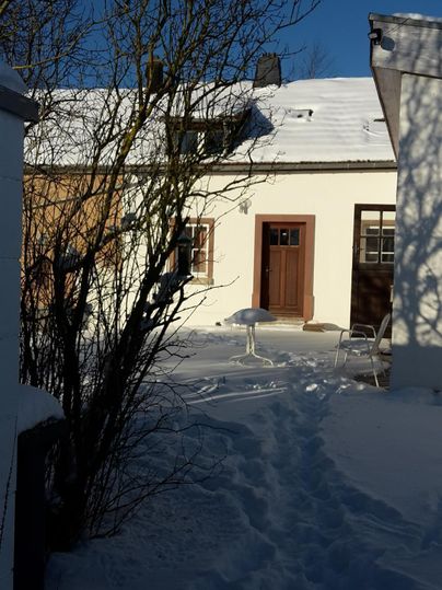 Een besneeuwde binnenplaats met een gezellig wit huis. De heldere blauwe lucht zorgt voor een vredige sfeer.