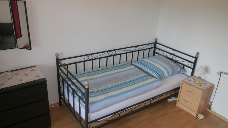 Ein einfaches Schlafzimmer mit einem metallenen Bett und einer Matratze mit Streifen. Neben dem Bett befindet sich ein Nachttisch und eine Kommode.