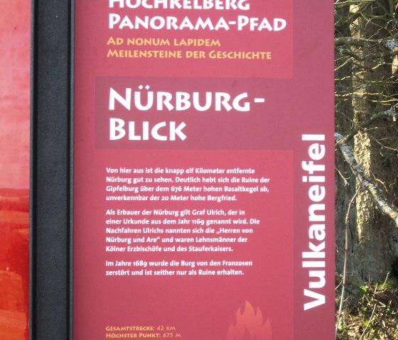 Red information board with text about the N&uuml;rburgblick on the Hochkelberg Panorama Trail. Contains historical information and hiking trail details., &copy; Touristik GmbH Gerolsteiner Land, Ute Klinkhammer