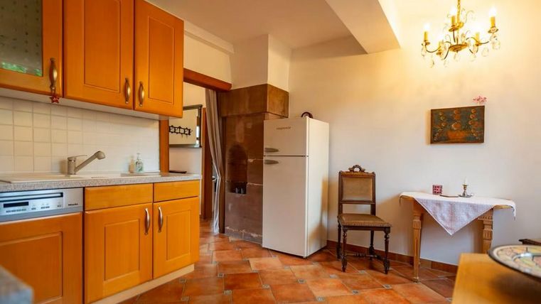 Eine gemütliche Küche mit orangefarbenen Schränken und einem weißen Kühlschrank. Auf einem kleinen Tisch steht eine Tischdecke und ein Stuhl steht daneben.