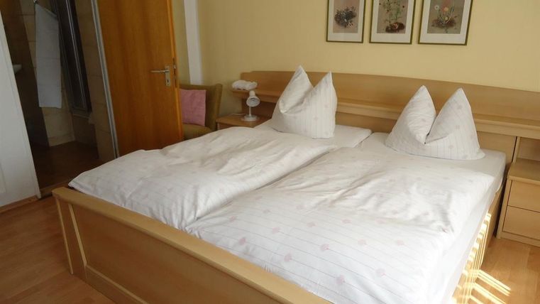 A cozy bedroom with a large double bed and two pillows. Three pictures hang on the wall, and the floor is made of wood.